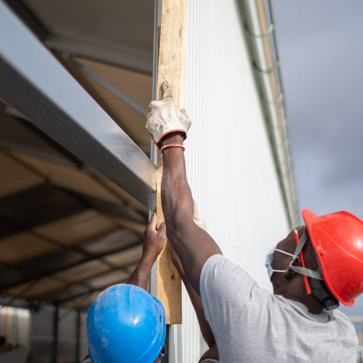 Two Afro-American builders wearing helmets and face masks while measuring the wall